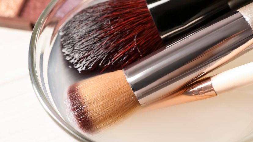 makeup brushes soaking in a shallow bowl of cleanser