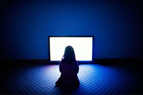 A girl sits in front of a television in a dark room. 