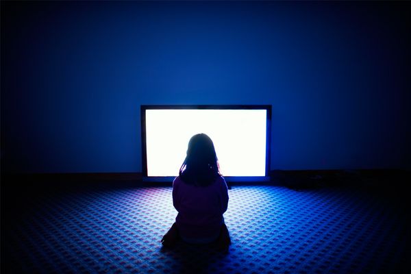 A girl sits in front of a television in a dark room. 