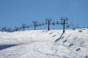 Winter tourists skiing down snowy resort slope via ski lift.