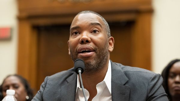 African businessman in suit speaks into microphone indoors.