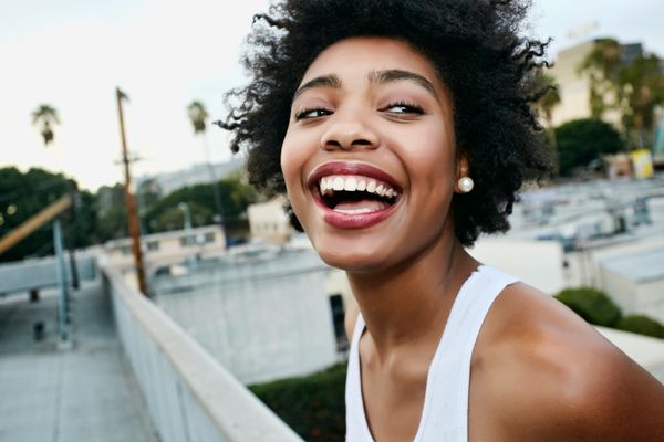 A woman standing atop an urban rooftop is laughing.