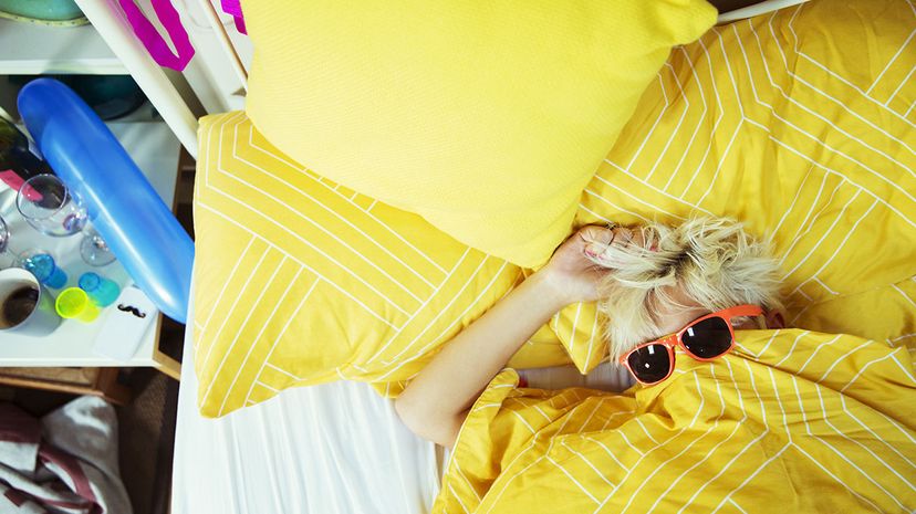 woman lying on yellow comforter, wearing sunglasses