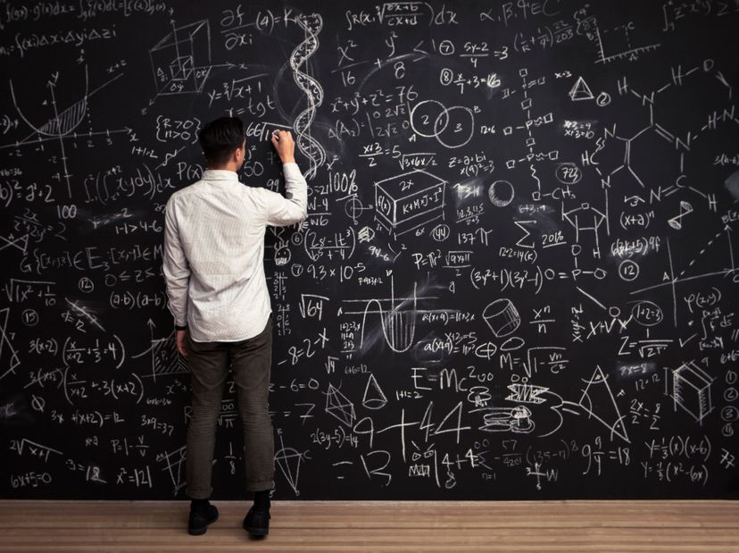 A young man writes on a chalkboard filled with mathematical equations, showing individuality, intelligence and creativity