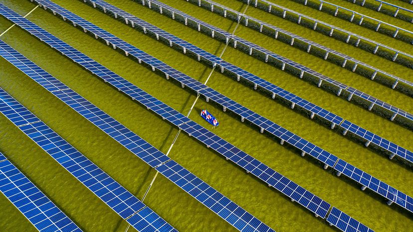 Three people in a boat check on rows of blue solar panels built in a pond.