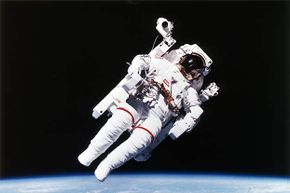 1984年，美国宇航员布鲁斯·麦克肯多斯(Bruce McCandless)穿上了第一套氮气推进、手动控制、无需系绳的宇航服。＂border=