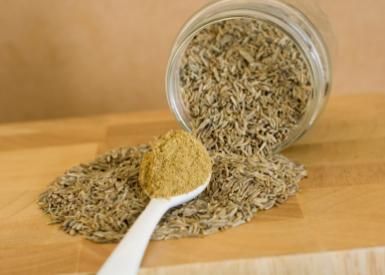 spoonful of ground cumin and whole cumin seeds spilling out of a jar