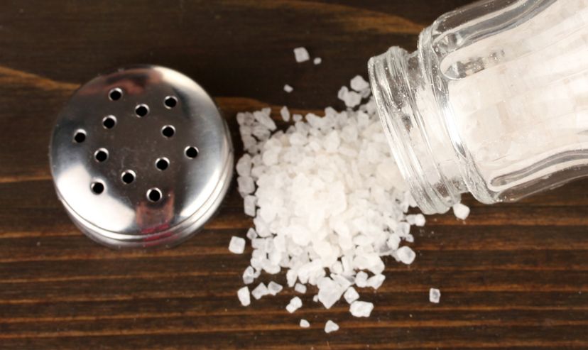 Salt spilling out of a sale shaker onto a wooden table.
