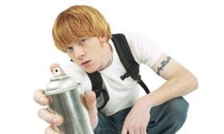 Teenage boy aiming a can of spray paint at the camera.