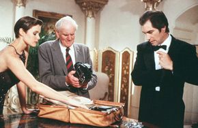 Bond (Timothy Dalton) meets with Q (Desmond Llewelyn) to receive his case full of gadgets in "License to Kill." The gadgets in this film include a camera that fires a deadly laser out of its flash component and a "signature gun" that Q has programmed for Bond's use alone.”width=