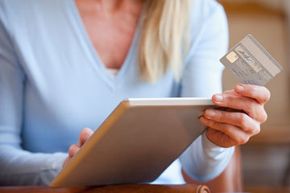 Woman holding credit card while looking at a tablet.