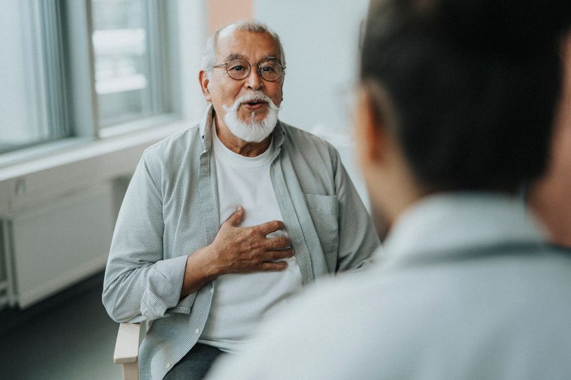 Elderly male patient receiving good news while sitting with doctor during consultation at hospital