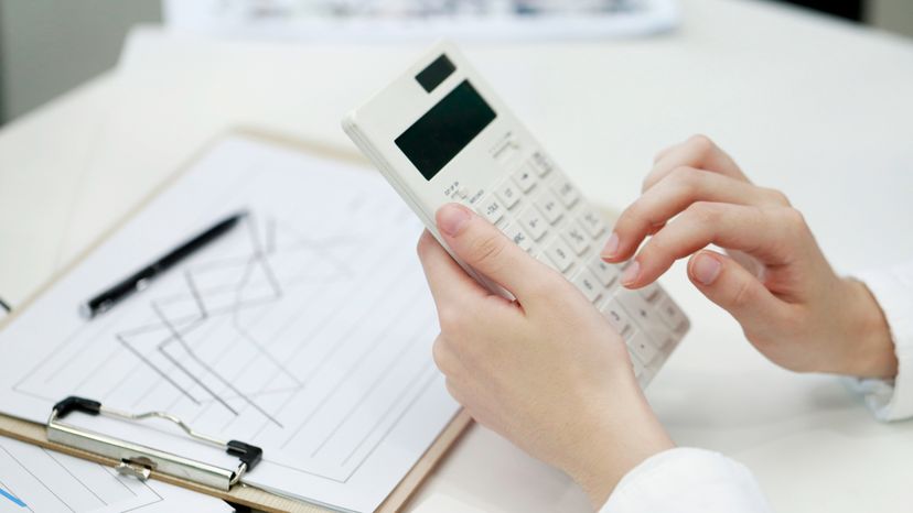 A woman using a white calculator on her desk.