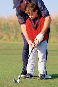 Adult assisting young boy with putting a golf ball on the green.