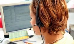 A woman wearing a telephone headset sits in front of a computer screen.