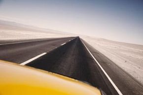 Yellow car speeding along a straight road in the desert.