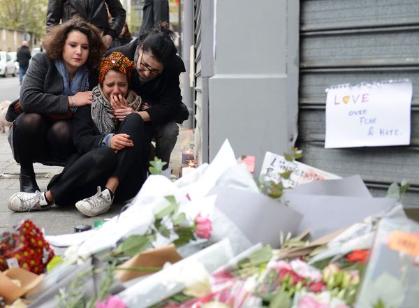 flowers in foreground and crying woman consoled by two people in background 