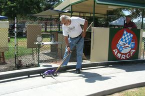 Ed Baynes readies a tether car for competition in the moment called "pushing off." The tether itself is faintly visible in the photo, attached to the frame of the car.”border=