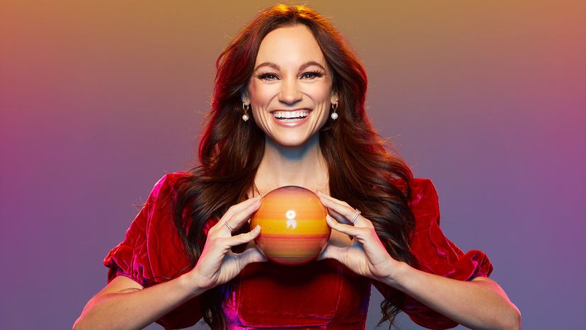 Emily Calandrelli in a red dress, smiling and holding a model of a planet.