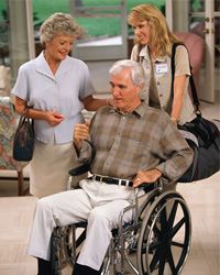 man in wheelchair accompanied by nurse and wife