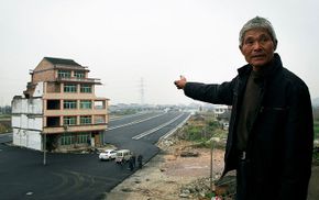 Luo Baogen points to his house which his provincial government built a road aound when he would not sell it to them. Tired of the traffic noise, he later sold his house to the government for slightly more money than he had orginally been offered.