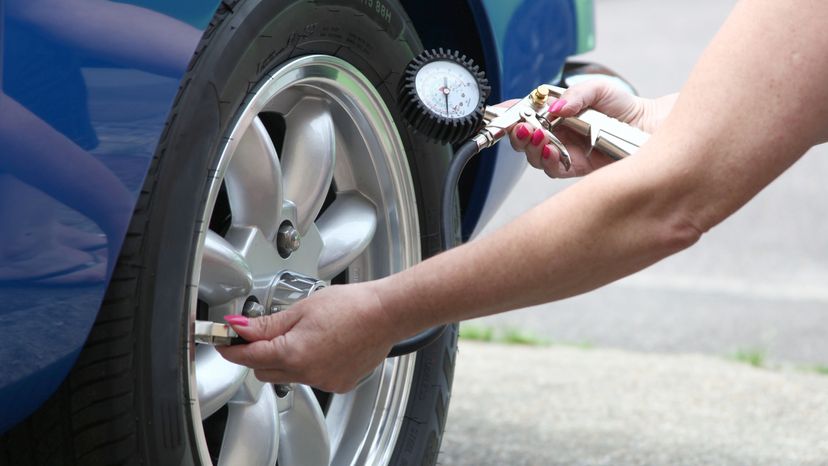 Woman Checking Tire Pressure with Gauge“width=