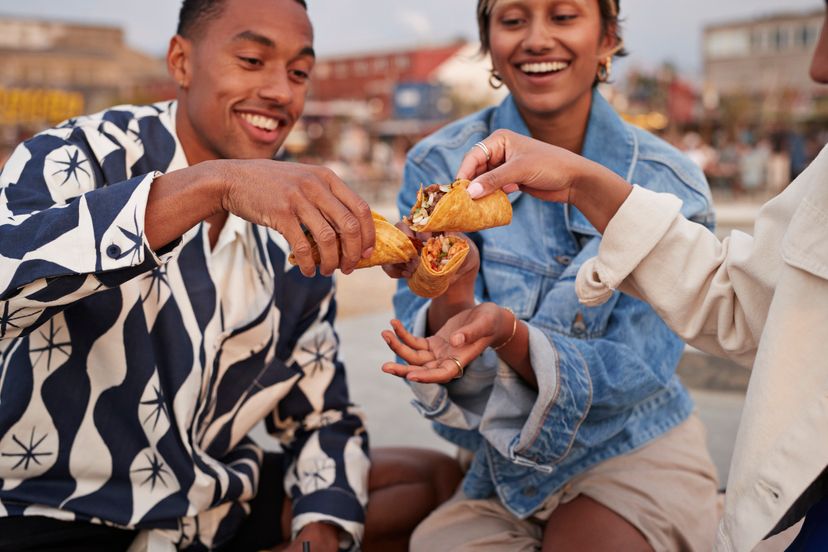 Happy multiracial friends toasting tempting tacos on promenade