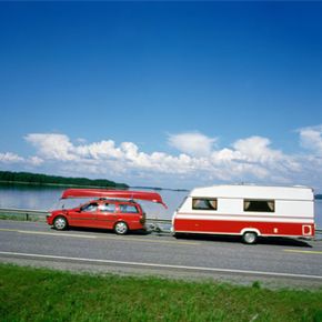 Car with a trailer hitched up drives alongside a body of water.