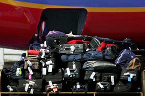 Baggage handlers load checked luggage aboard a Southwest Airlines jet as a tram carrying more bags passes in the foreground at Los Angeles International Airport.