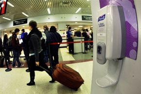 A traveler wheels luggage past one of many hand sanitizer dispensers hung on walls at Logan International Airport in Boston.