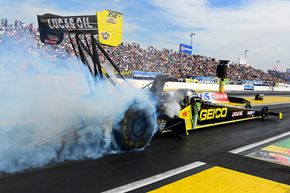 The GEICO Top Fuel dragster performs a smoky burnout with driver Richie Crampton at the wheel.