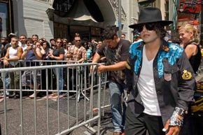 在好莱坞星光大道的好莱坞星光大道上，一名迈克尔·杰克逊的模仿者走在等待向迈克尔·杰克逊的星星致敬的粉丝前面。＂border=