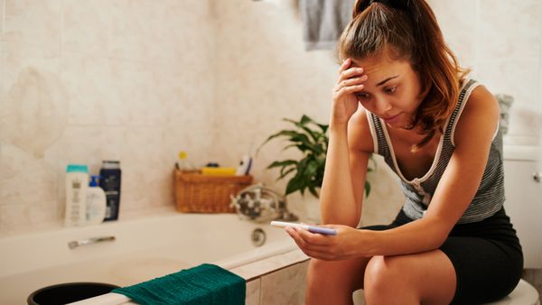 A distressed young woman taking a pregnancy test in the bathroom at home