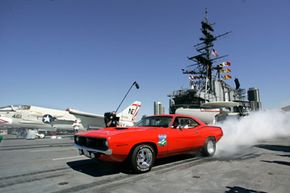 A Chevrolet Camaro burns its tires alongside a Navy fighter jet during a demonstration on the flight deck of the USS Midway in San Diego, Calif.