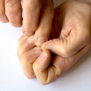 A man picking at his already-damaged fingernails.