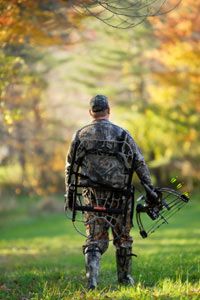 Hunter walking with tree stand and bow.