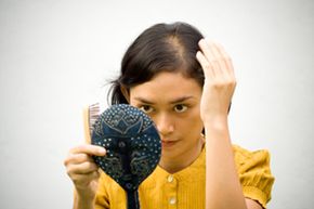 woman looks at bald spot in mirror