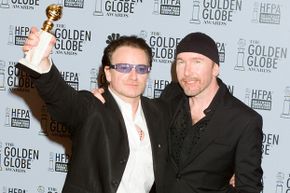 Musician Bono holds up an award while standing next to The Edge (also a musician).