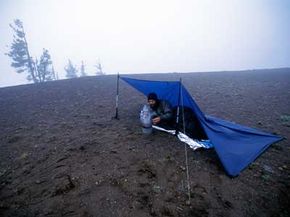 一名徒步旅行者在太平洋波峰步道上的篷布下停下来休息。防水布是轻巧的避难所。“border=