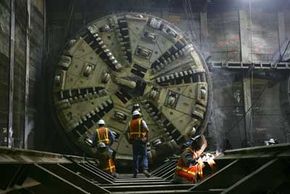 As workers follow a massive tunnel-boring machine, they put the finishing touches on the support structure for a train tunnel.