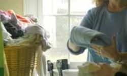 A woman folds a item of clothing next to a full laundry basket.