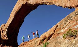 A family of four hikes under an arch in Moab, Utah.