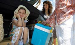 A girl's father takes the family cooler out of the car.