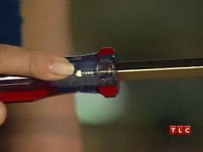 Person holding a dark colored screwdriver with red stripes on it.