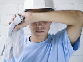 A Young worker holding gloves and wiping his forehead with his arm