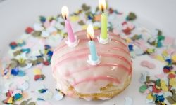 A donut with three birthday candles, surrounded by confetti.