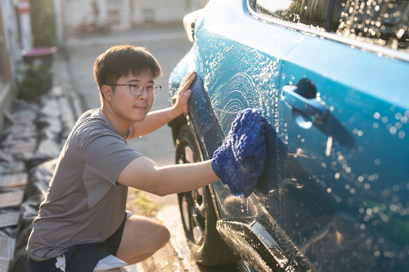 Young asian adult man washing car in yard