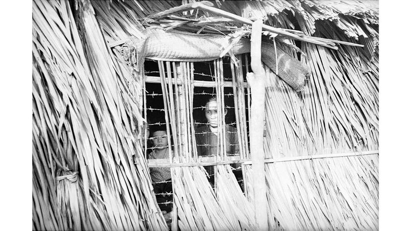 Chapelle's haunting images show the horrors of war from all sides. Here, two Viet Cong prisoners are seen peering through a window covered in barbed wire in a structure built of bamboo and grass.