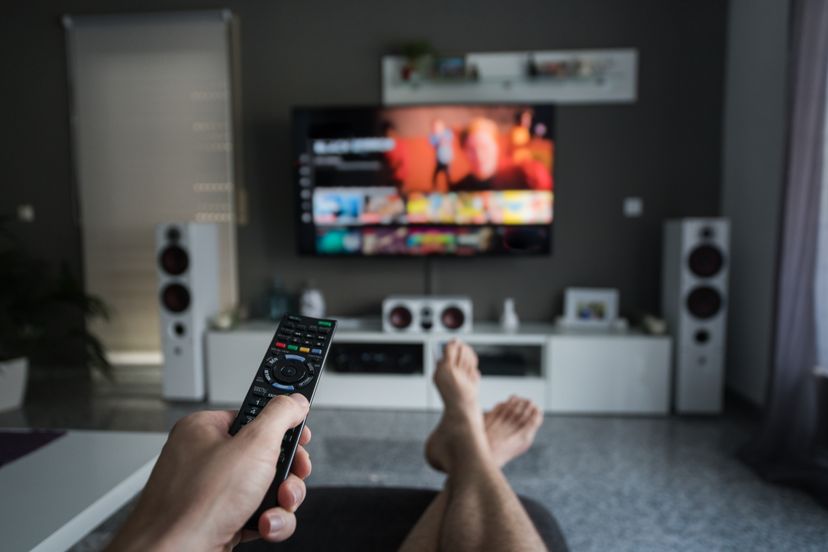 A young man is browsing through television channels with a remote control.