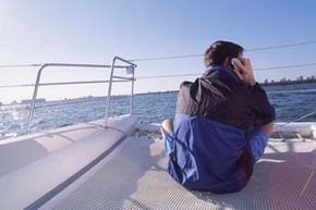 男子在船上使用移动设备。”width=